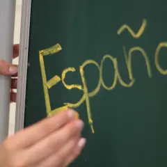 Ręka pisze kredą na tablicy "Español". Może to być symbol wniosku rodzica o zwolnienie z drugiego języka obcego.