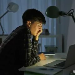 Chłopiec przy biurku, zmęczony i przygnębiony, doświadcza cyberprzemocy w szkole.