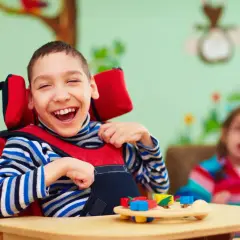 Uśmiechnięty chłopiec w fotelu, który potrzebuje wsparcia. Nauczyciel wspomagający jest dla dzieci z orzeczeniem o potrzebie kształcenia specjalnego.