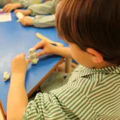 Dziecko w zielono-białej koszulce lepi z plasteliny. To przykład kształcenia specjalnego w przedszkolu, gdzie rozwija się kreatywność.