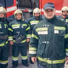 Pięciu strażaków w mundurach i kaskach przed wozem strażackim. Zastanawiasz się, ile zarabia strażak zawodowy?