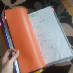Ręka trzyma pomarańczową okładkę segregatora, odsłaniając zeszyt z notatkami i schematem. Widać nagłówek "FORMATYKA" i zasady prowadzenia zeszytu.