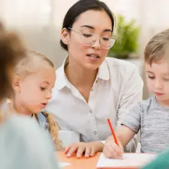 Nauczycielka w okularach pomaga dzieciom rysować. Po kursie można pracować w przedszkolu, ucząc maluchy.