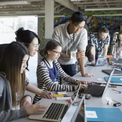 Nauczyciel wspomagający z kwalifikacjami pomaga uczniom przy komputerach. Dzieci uczą się programowania i robotyki.