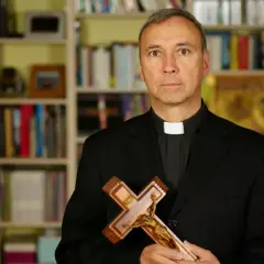 Duchowny z krzyżem w dłoniach, na tle regałów z książkami. Zastanawia się, od kiedy religia wlicza się do średniej.