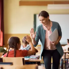 Nauczycielka daje piątkę uczennicy, która z radością odpowiada. Czy zadania domowe są obowiązkowe? Ta interakcja sugeruje, że nauka może być przyjemna!