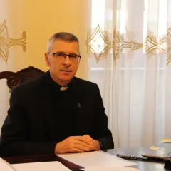 Duchowny w okularach siedzi przy biurku, pracując nad dokumentami. Pokazuje, co można robić po teologii: nauczanie, pisanie, doradztwo.
