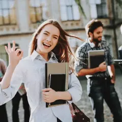 Uśmiechnięta studentka z notatnikami pokazuje znak OK. Pokazuje, jakie są perspektywy dla osób z wykształceniem humanistycznym – świetlane!