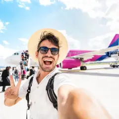 Szczęśliwy turysta z plecakiem i kapeluszem robi selfie na tle samolotu. To dopiero początek przygody, co po turystyce i rekreacji!