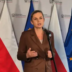 Ministerka przemawia o edukacji seksualnej w szkołach, stojąc przed flagami Polski i UE.