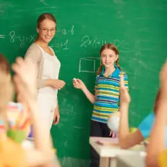 Nauczycielka i uczennica przy tablicy, gdzie rozwiązują zadania. To obrazek z życia szkoły, gdzie ocena pracy nauczyciela jest ważna, zgodnie z rozporządzeniem.