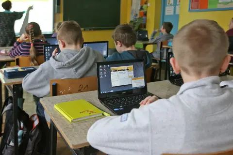 Dzieci w szkole pracują na laptopach. Nauczycielka tłumaczy materiał. Ile czasu ma nauczyciel na sprawdzenie sprawdzianu?
