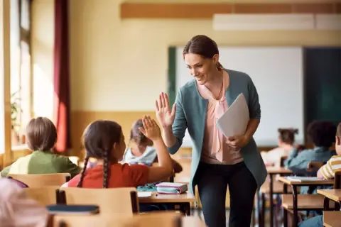 Nauczycielka daje piątkę uczennicy, która z radością odpowiada. Czy zadania domowe są obowiązkowe? Ta interakcja sugeruje, że nauka może być przyjemna!
