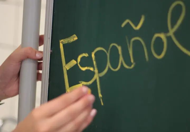 Ręka pisze kredą na tablicy "Español". Może to być symbol wniosku rodzica o zwolnienie z drugiego języka obcego.