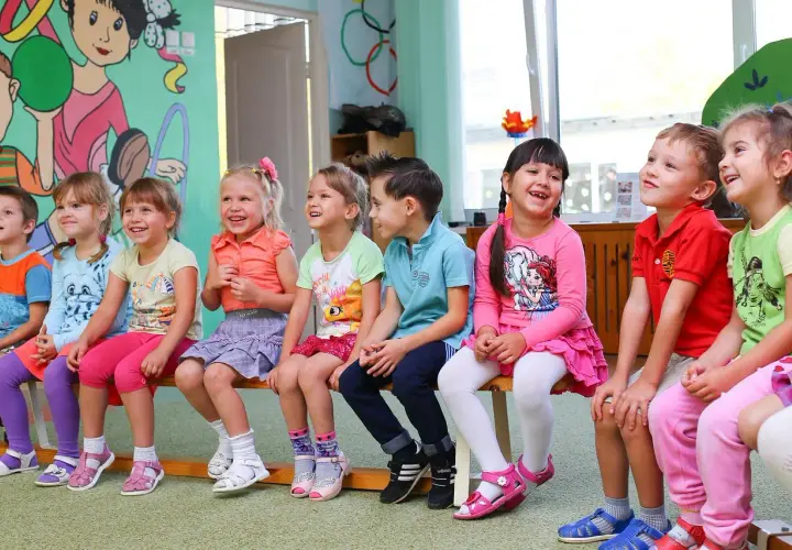 Uśmiechnięte dzieci siedzą w przedszkolu. Od ilu lat można tu chodzić?