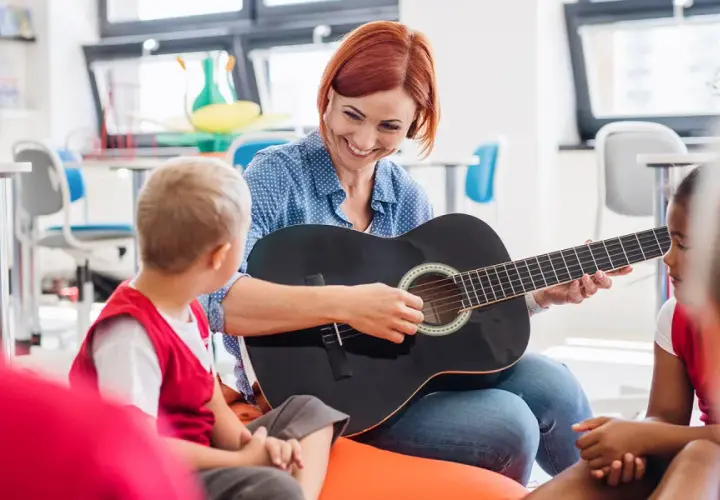 Nauczycielka gra na gitarze dla dzieci, tworząc zindywidualizowaną ścieżkę kształcenia. Przykłady takiej nauki to muzyka.
