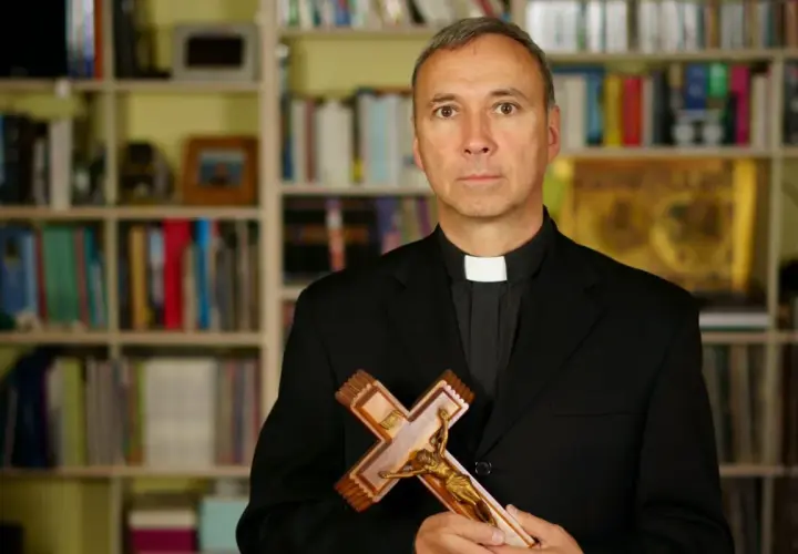 Duchowny z krzyżem w dłoniach, na tle regałów z książkami. Zastanawia się, od kiedy religia wlicza się do średniej.