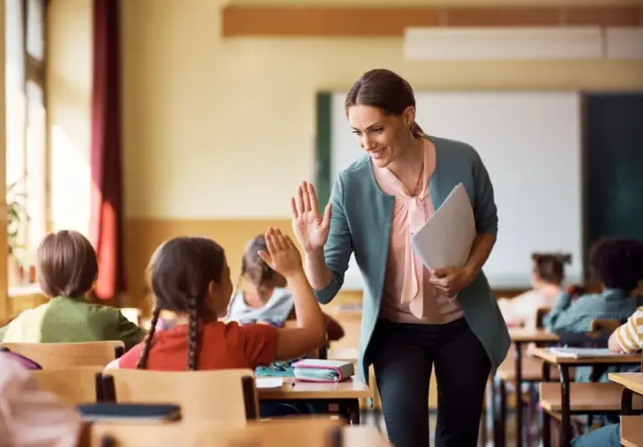 Nauczycielka daje piątkę uczennicy, która z radością odpowiada. Czy zadania domowe są obowiązkowe? Ta interakcja sugeruje, że nauka może być przyjemna!
