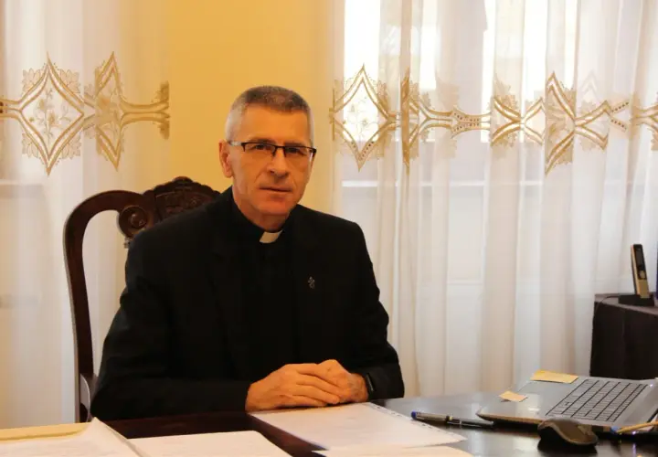 Duchowny w okularach siedzi przy biurku, pracując nad dokumentami. Pokazuje, co można robić po teologii: nauczanie, pisanie, doradztwo.