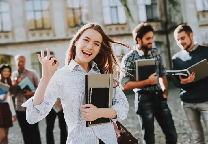 Uśmiechnięta studentka z notatnikami pokazuje znak OK. Pokazuje, jakie są perspektywy dla osób z wykształceniem humanistycznym – świetlane!