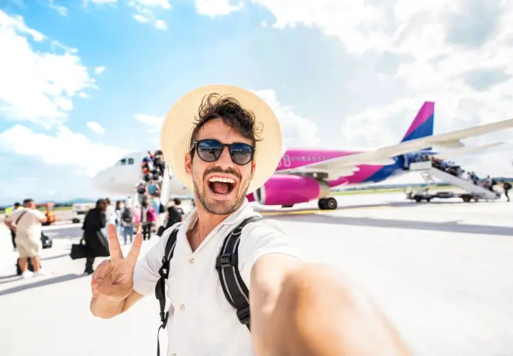 Szczęśliwy turysta z plecakiem i kapeluszem robi selfie na tle samolotu. To dopiero początek przygody, co po turystyce i rekreacji!