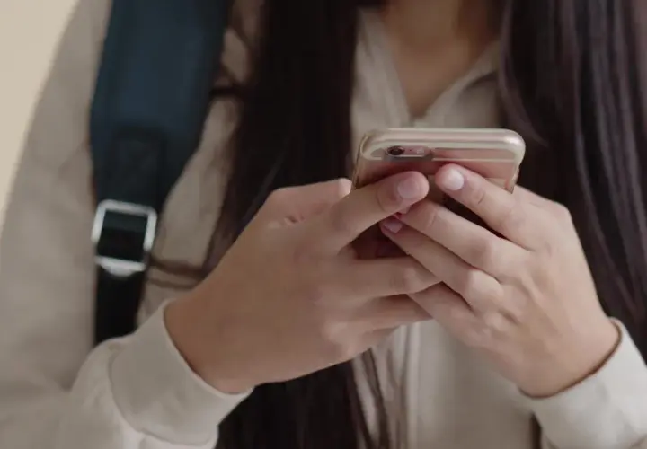 Dłonie uczennicy trzymają telefon, mimo że obowiązuje zakaz telefonów w szkole.
