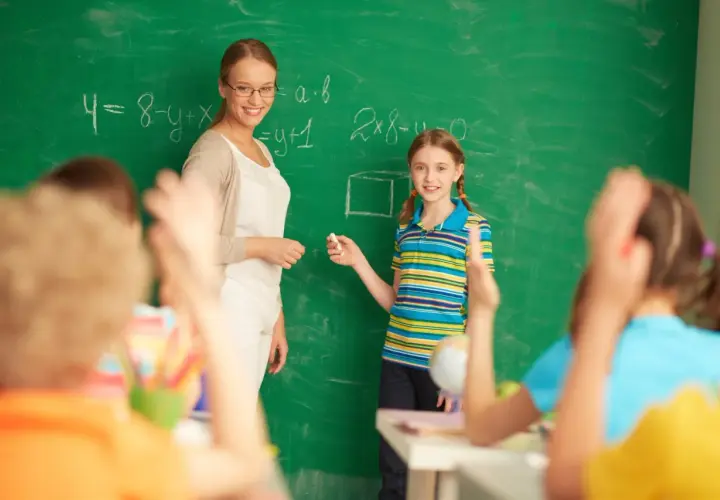 Nauczycielka i uczennica przy tablicy, gdzie rozwiązują zadania. To obrazek z życia szkoły, gdzie ocena pracy nauczyciela jest ważna, zgodnie z rozporządzeniem.