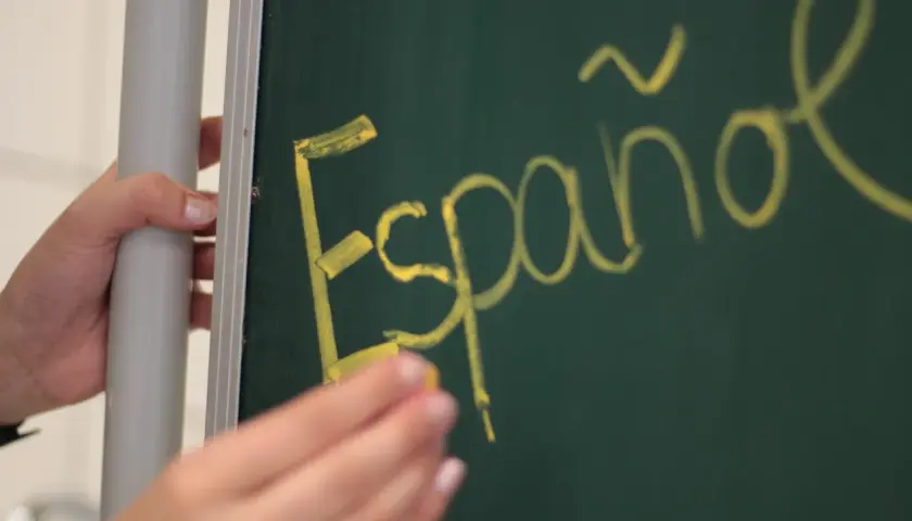 Ręka pisze kredą na tablicy "Español". Może to być symbol wniosku rodzica o zwolnienie z drugiego języka obcego.
