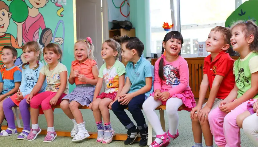 Uśmiechnięte dzieci siedzą w przedszkolu. Od ilu lat można tu chodzić?