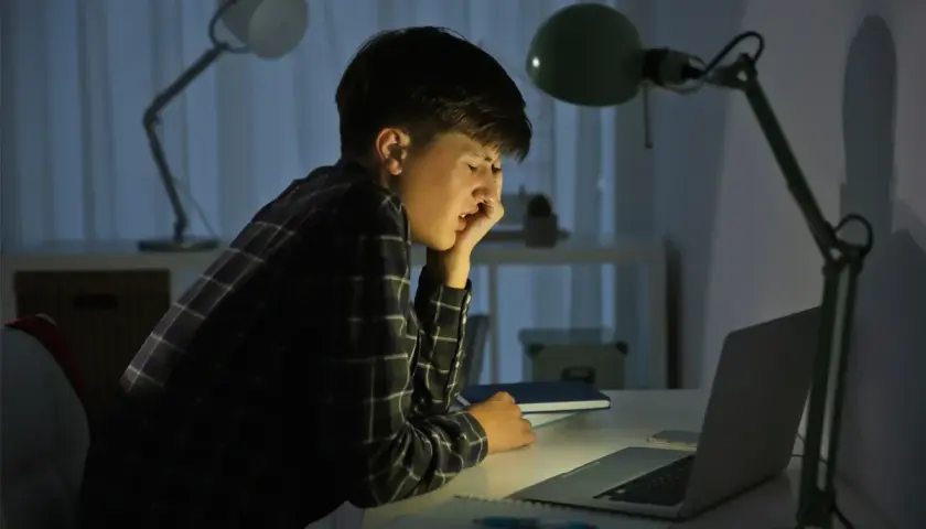 Chłopiec przy biurku, zmęczony i przygnębiony, doświadcza cyberprzemocy w szkole.