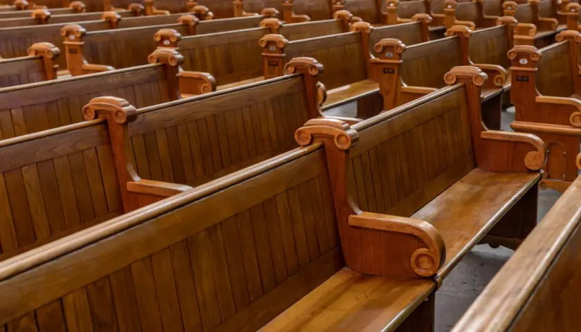 Puste, drewniane ławki w kościele, symbolizujące rezygnację z religii i pustkę po odejściu wiary.