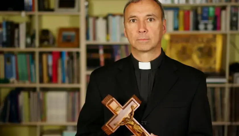 Duchowny z krzyżem w dłoniach, na tle regałów z książkami. Zastanawia się, od kiedy religia wlicza się do średniej.