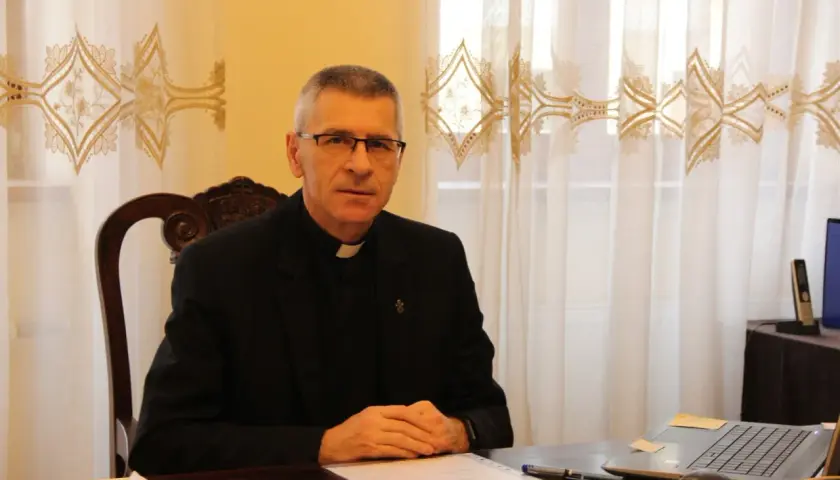 Duchowny w okularach siedzi przy biurku, pracując nad dokumentami. Pokazuje, co można robić po teologii: nauczanie, pisanie, doradztwo.