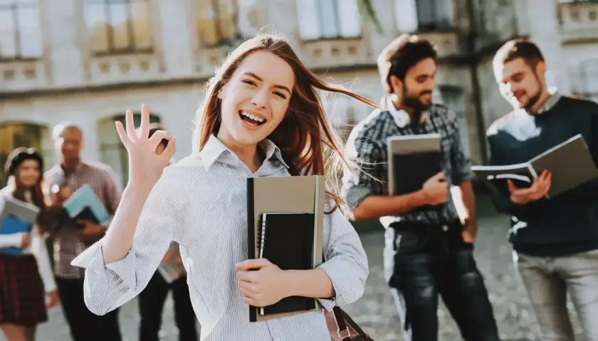 Uśmiechnięta studentka z notatnikami pokazuje znak OK. Pokazuje, jakie są perspektywy dla osób z wykształceniem humanistycznym – świetlane!