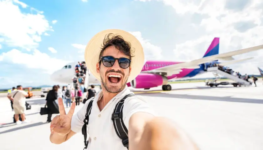 Szczęśliwy turysta z plecakiem i kapeluszem robi selfie na tle samolotu. To dopiero początek przygody, co po turystyce i rekreacji!