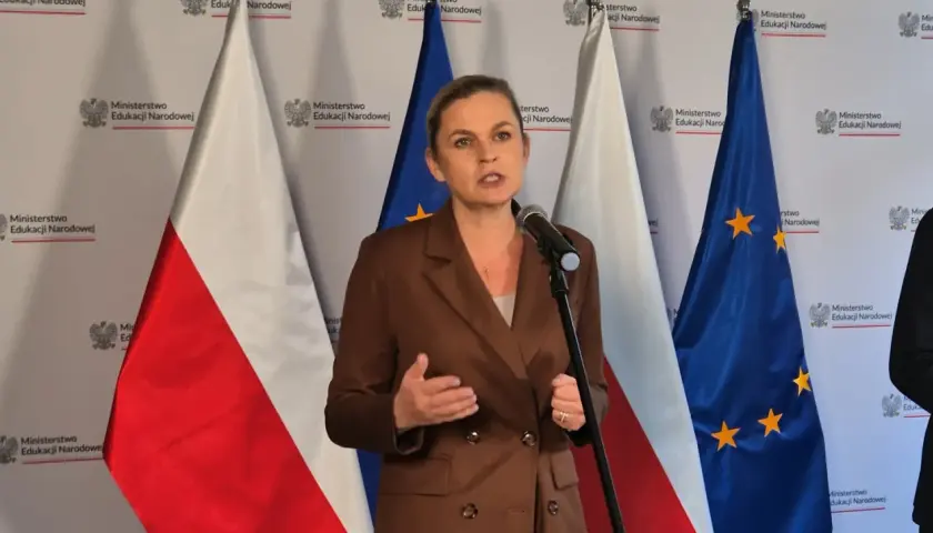 Ministerka przemawia o edukacji seksualnej w szkołach, stojąc przed flagami Polski i UE.