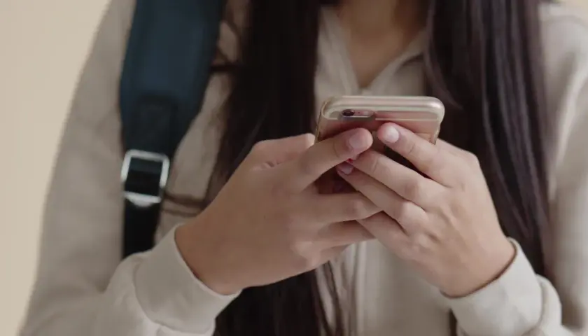 Dłonie uczennicy trzymają telefon, mimo że obowiązuje zakaz telefonów w szkole.