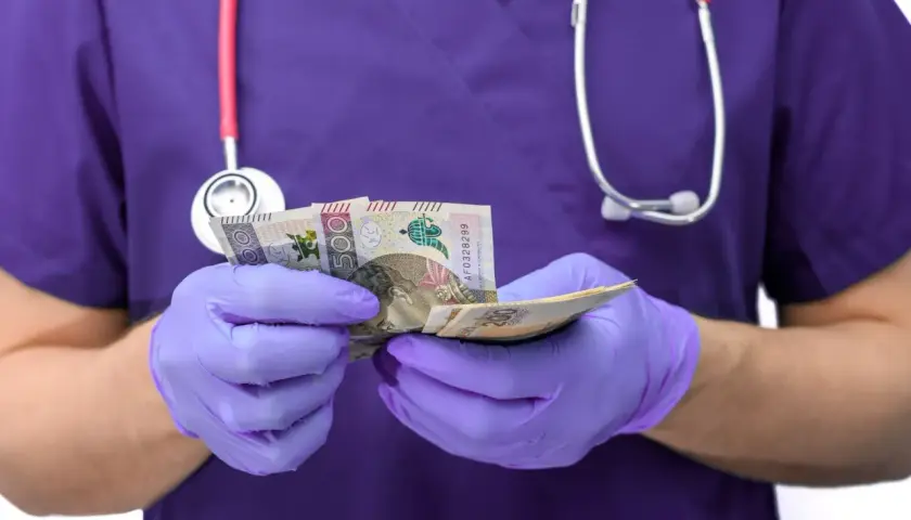 Pielęgniarka w fioletowym uniformie i rękawiczkach liczy pieniądze. Ile zarabia pielęgniarka po studiach?