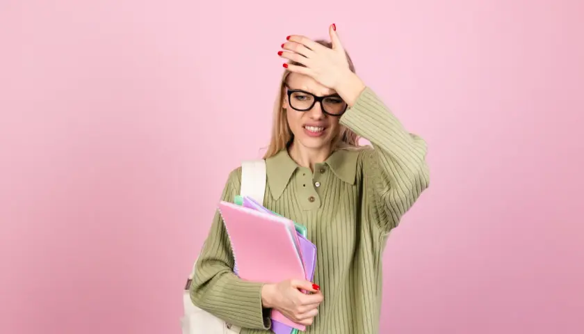 Studentka z zeszytami w ręku, zmartwiona, z dłonią na czole. Chyba zapomniała o zaliczeniu, a czeka ją minimalna frekwencja w szkole.