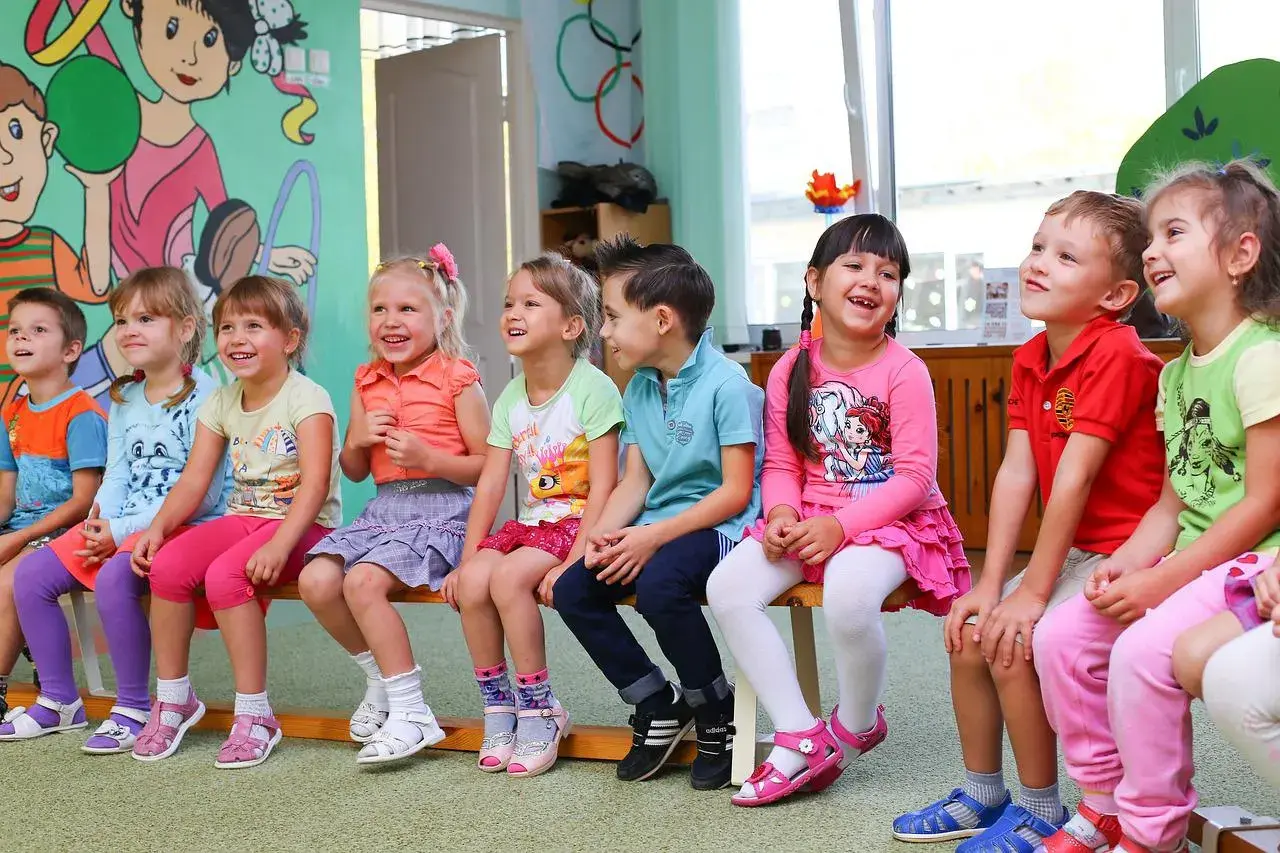 Uśmiechnięte dzieci siedzą w przedszkolu. Od ilu lat można tu chodzić?