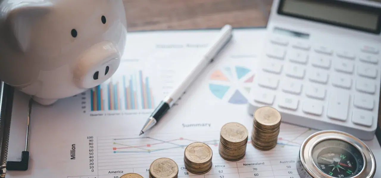 Świnka-skarbonka, monety, kalkulator i kompas na wykresach. Planowanie przyszłości po studiach finanse i rachunkowość.
