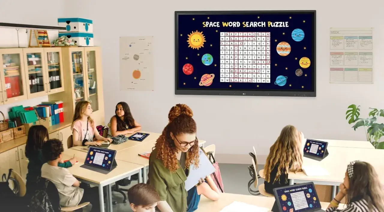Nowoczesna klasa szkolna z uczniami rozwiązującymi kosmiczną łamigłówkę na tabletach i interaktywnym ekranie.