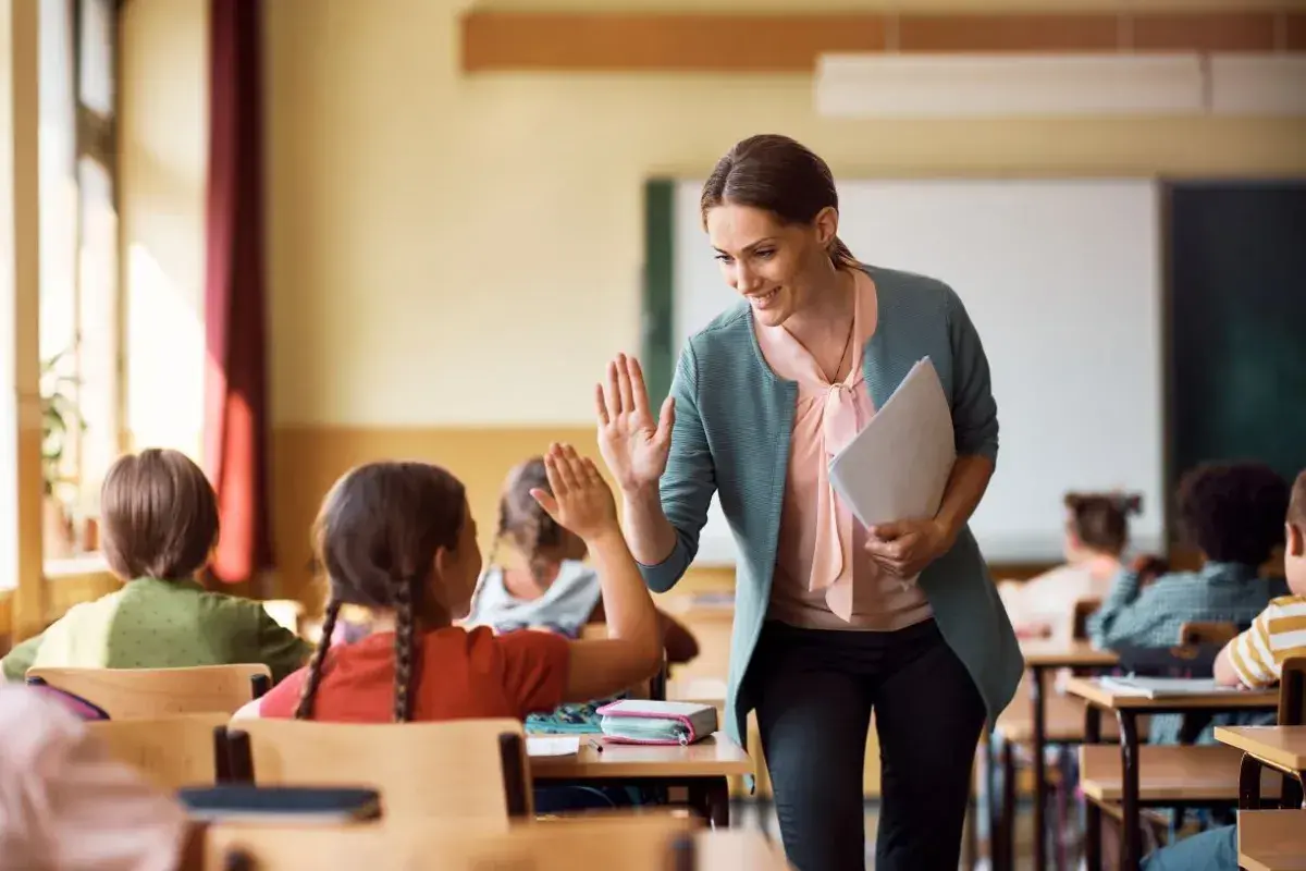 Nauczycielka daje piątkę uczennicy, która z radością odpowiada. Czy zadania domowe są obowiązkowe? Ta interakcja sugeruje, że nauka może być przyjemna!
