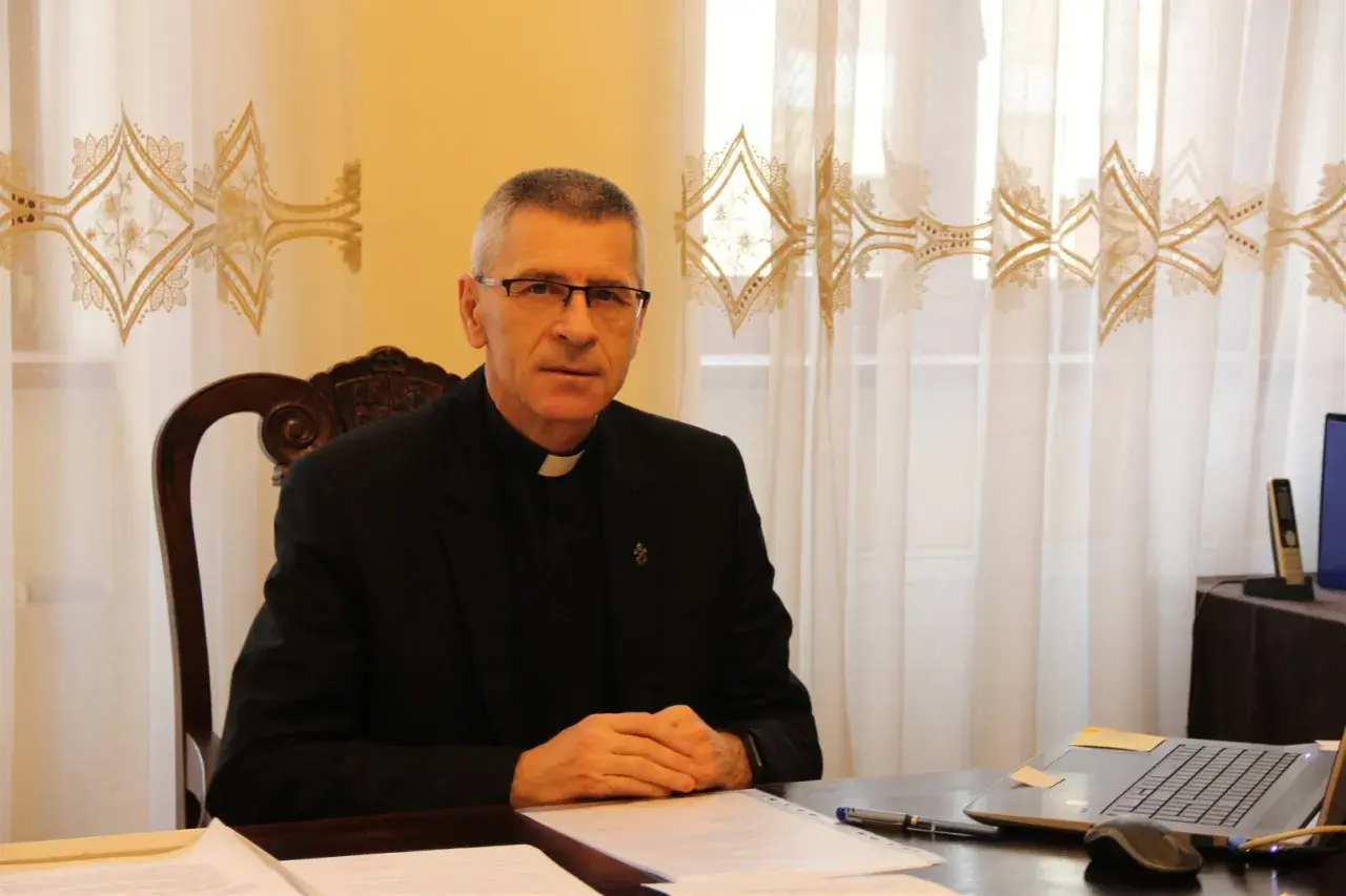Duchowny w okularach siedzi przy biurku, pracując nad dokumentami. Pokazuje, co można robić po teologii: nauczanie, pisanie, doradztwo.