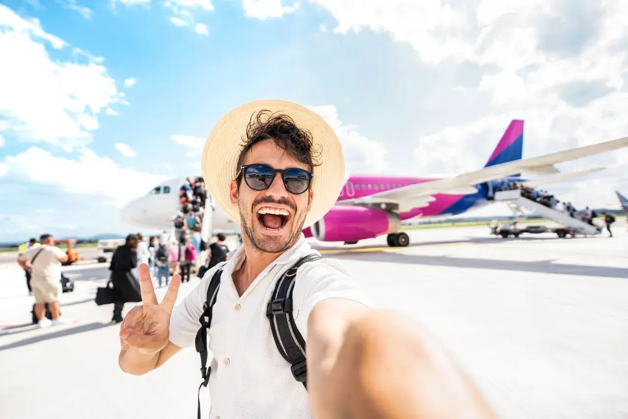 Szczęśliwy turysta z plecakiem i kapeluszem robi selfie na tle samolotu. To dopiero początek przygody, co po turystyce i rekreacji!