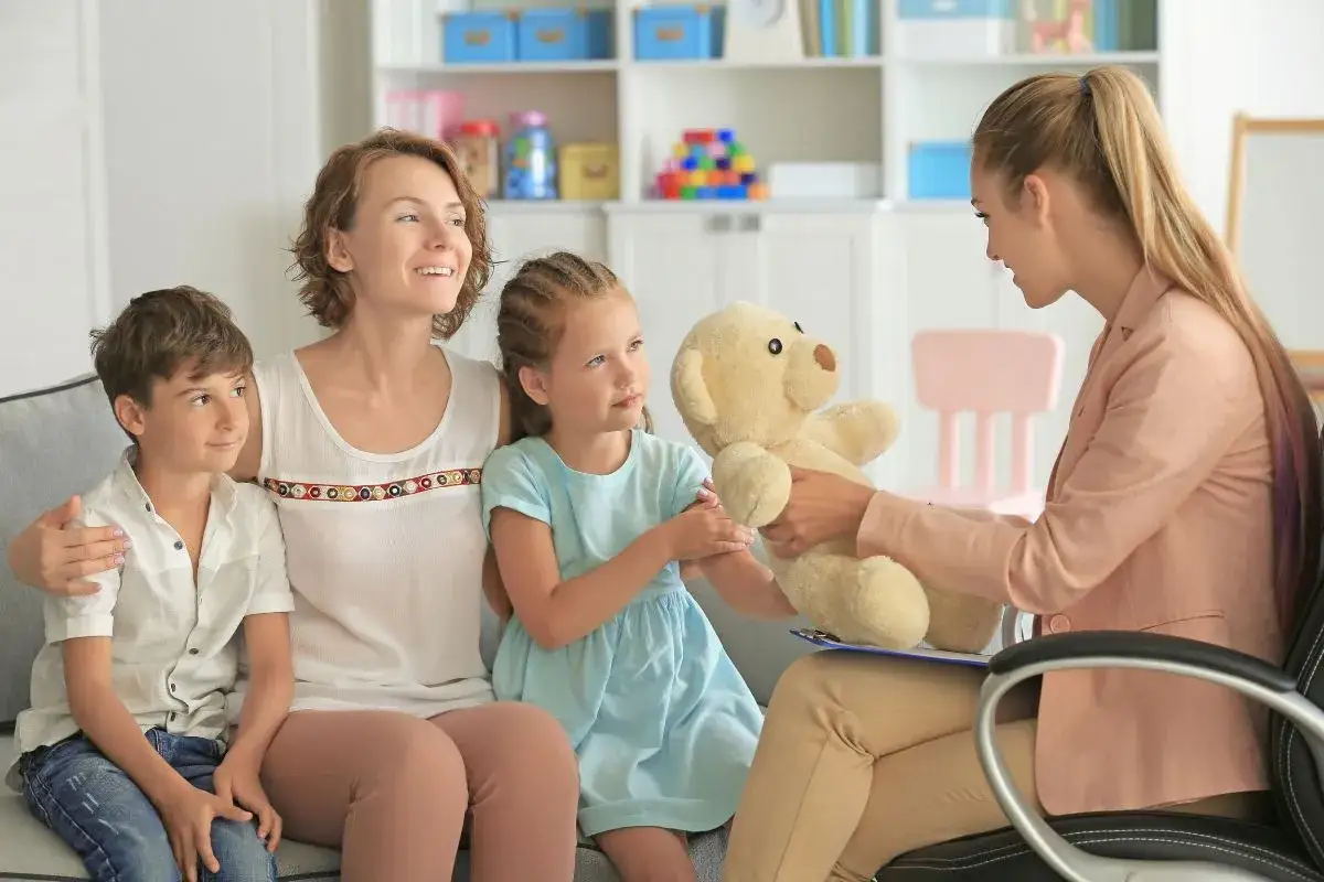 Terapeuta pokazuje miś dziecku, stosując metody pracy z dzieckiem autystycznym. Rodzina uczestniczy w sesji.