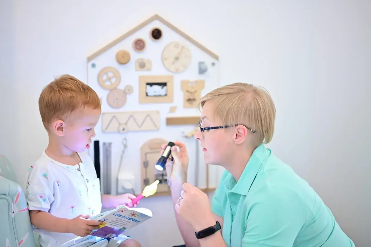 Oligofrenopedagog, pedagog specjalny, z latarką rozświetla dziecku książkę. Zabawa i nauka w przyjaznym gabinecie.