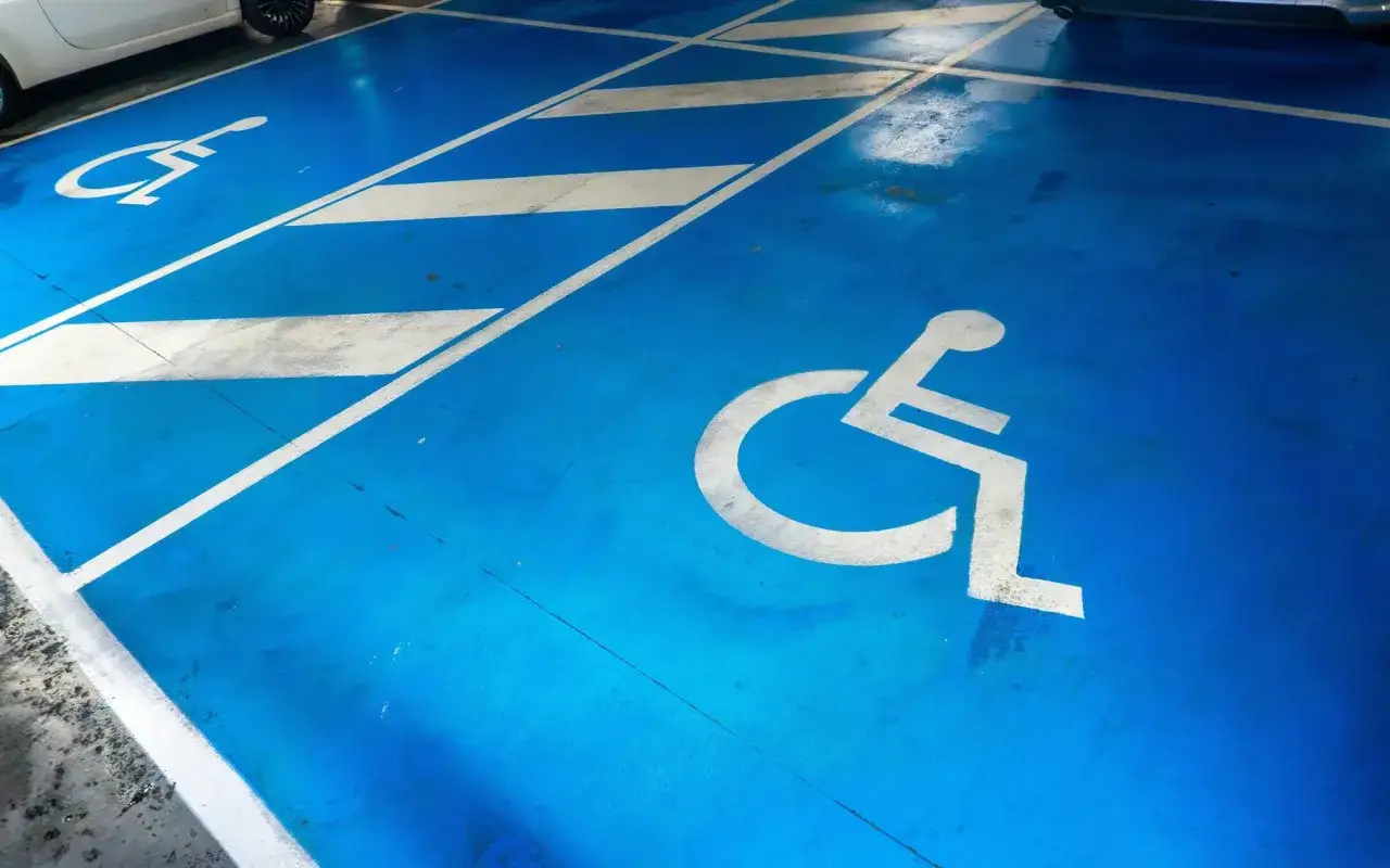 Niebieski parking z białymi symbolami wózka inwalidzkiego, wskazującymi miejsca dla osób z niepełnosprawnościami sprzężone rodzaje.