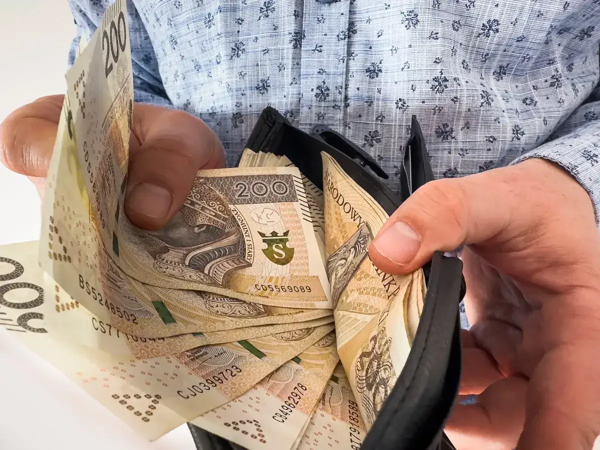 Ręce trzymają portfel z banknotami 200 zł. To może być świadczenie na start dla nauczycieli, wspierające ich na początku kariery.