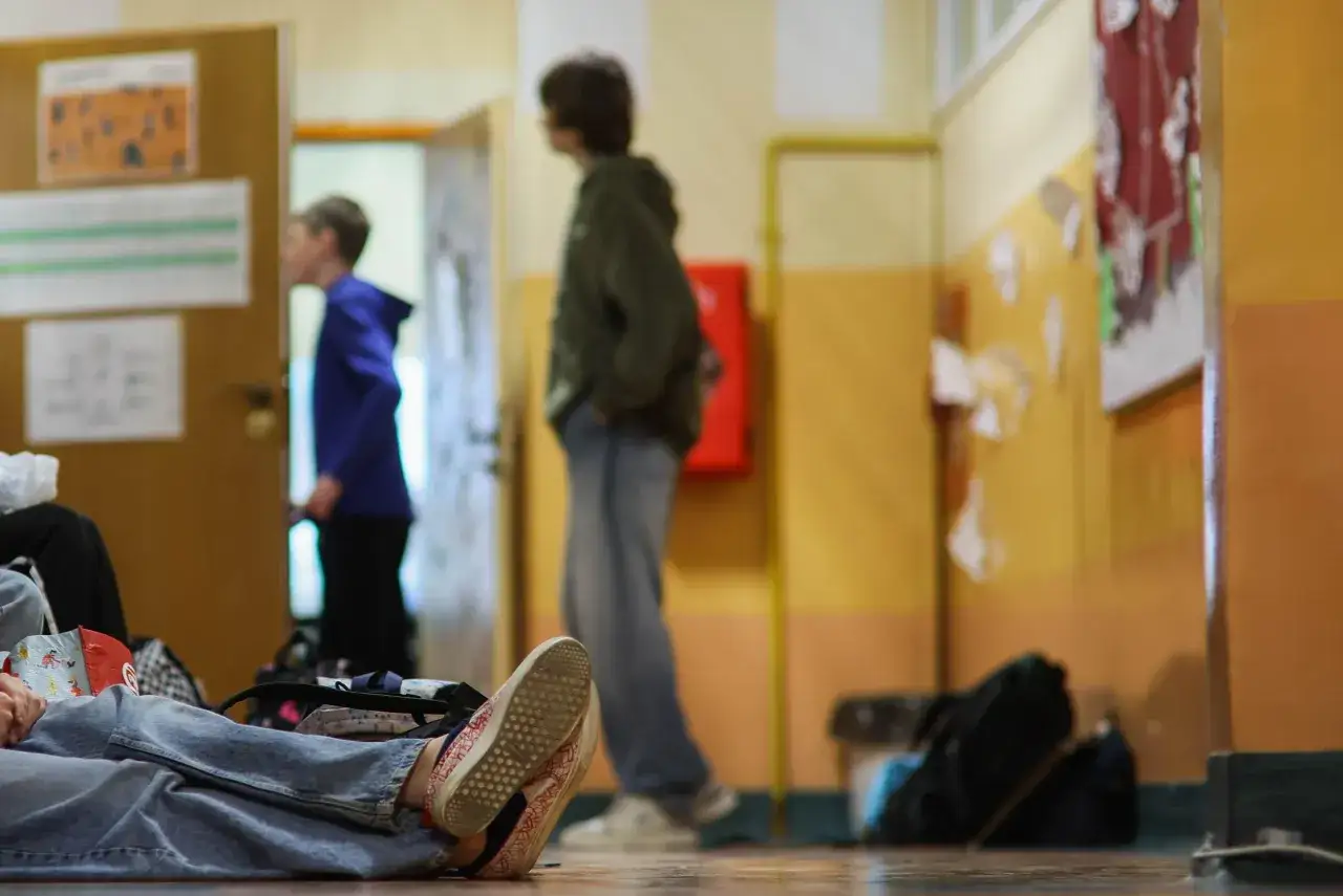 Uczeń leży na podłodze korytarza szkolnego, podczas gdy inni chodzą. Może to być dzień wolny od zajęć, czyli nieobecność w szkole.